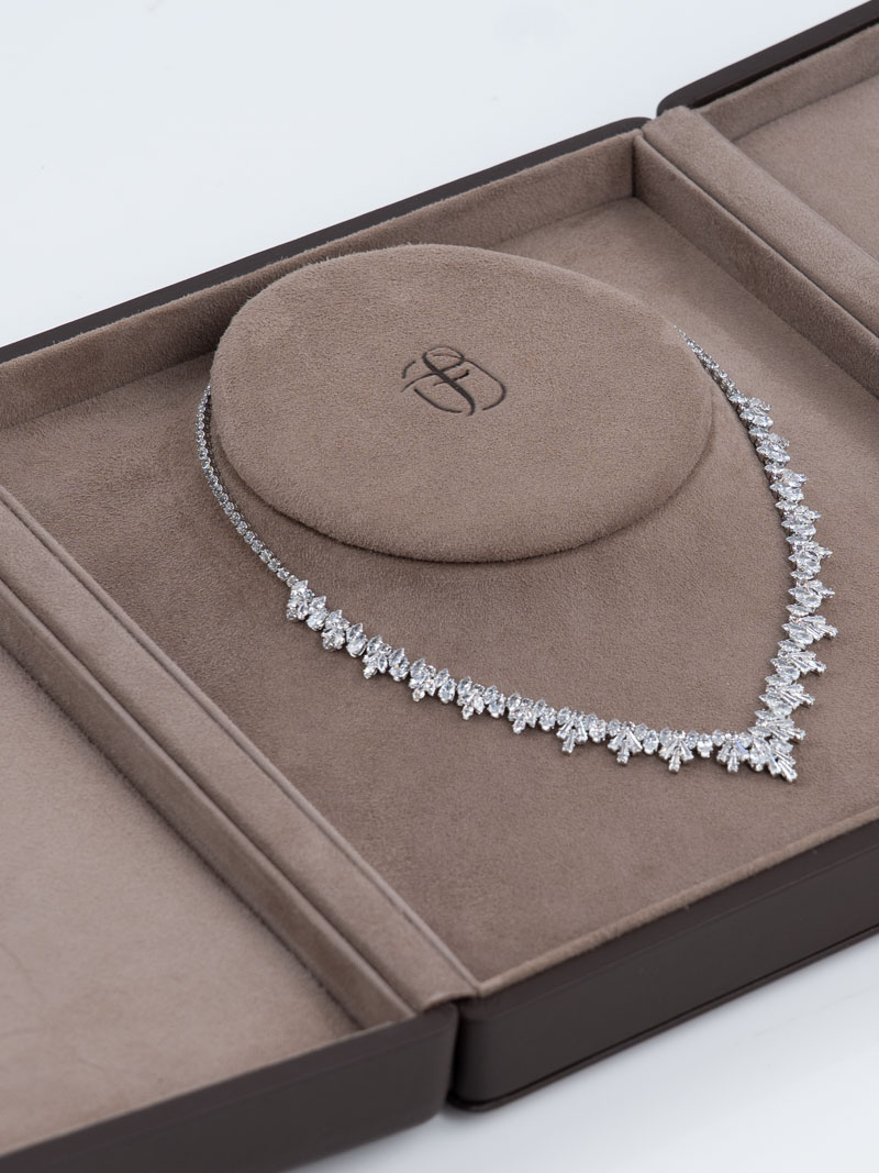 Détail d'un écrin Fleur de Luxe ouvert en marron avec insert de buste et logo en relief avec collier de brillants