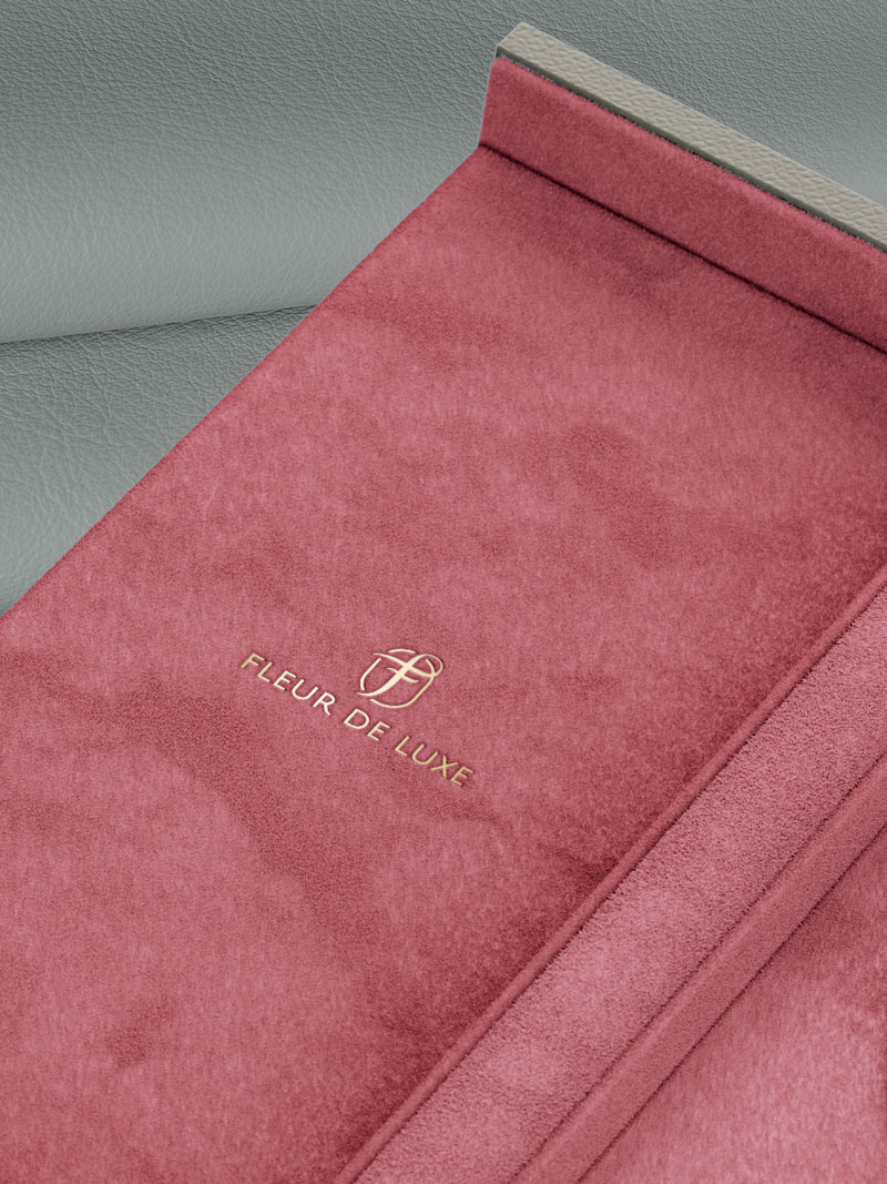 Détail d'un écrin Fleur de Luxe avec logo gaufré à la feuille d'or en Rosé-fluo, posé sur du cuir de veau en Grey-Brown